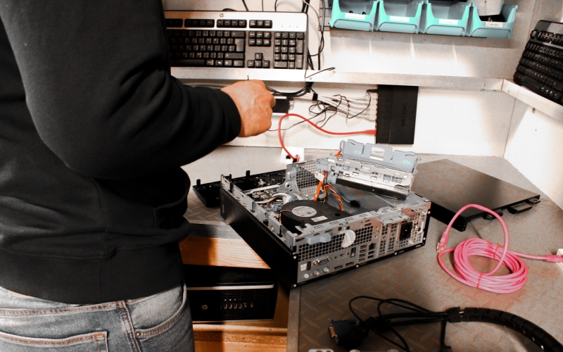 Een medewerker van Aronto verwijdert zorgvuldig onderdelen uit een pc, als onderdeel van het recyclingproces waarbij bruikbare componenten worden hergebruikt of milieuvriendelijk verwerkt.